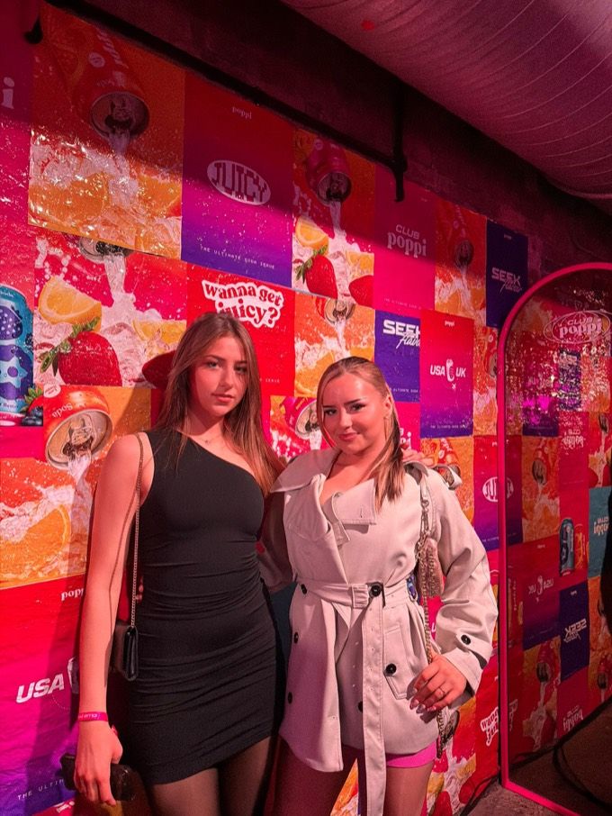 Two RealQuick Media creators posing against the Club Poppi branded wall at the London launch party