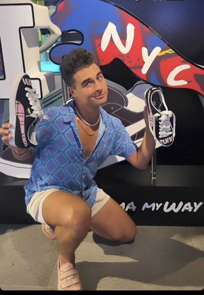 Creator holding two custom Puma sneakers in front of the Puma NYC mural